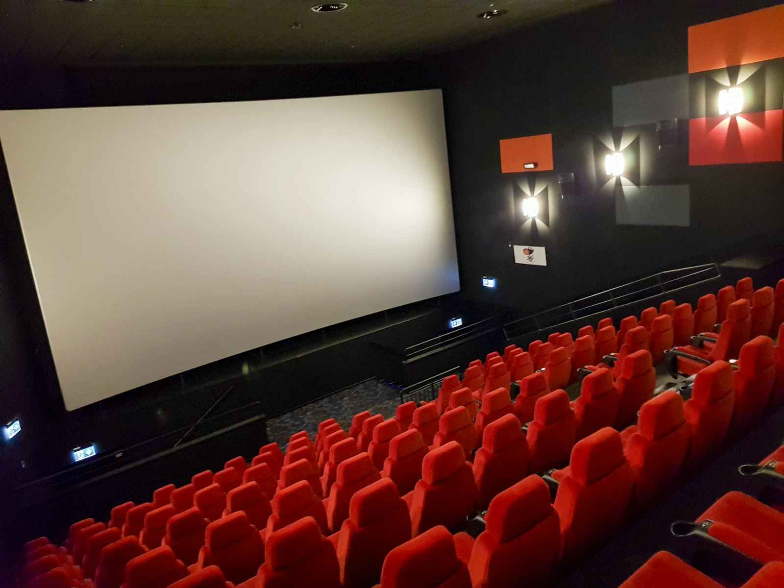 Sala de cinema vazia com poltronas vermelhas e tela de projeção